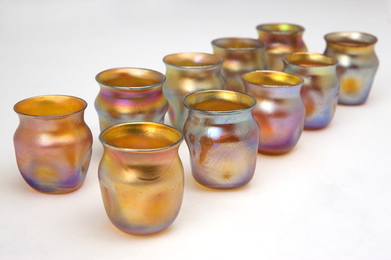Ten Tiffany Studios Favrile cordials or toothpick: Circa 1900, each with etched signature ''L.C.T. Favrile'' and numbered ''105'', each of gold iridescent glass, each with a circular flared rim over squared, pinched sides, 10 pcs, 1.75'' H x 1.625'' D