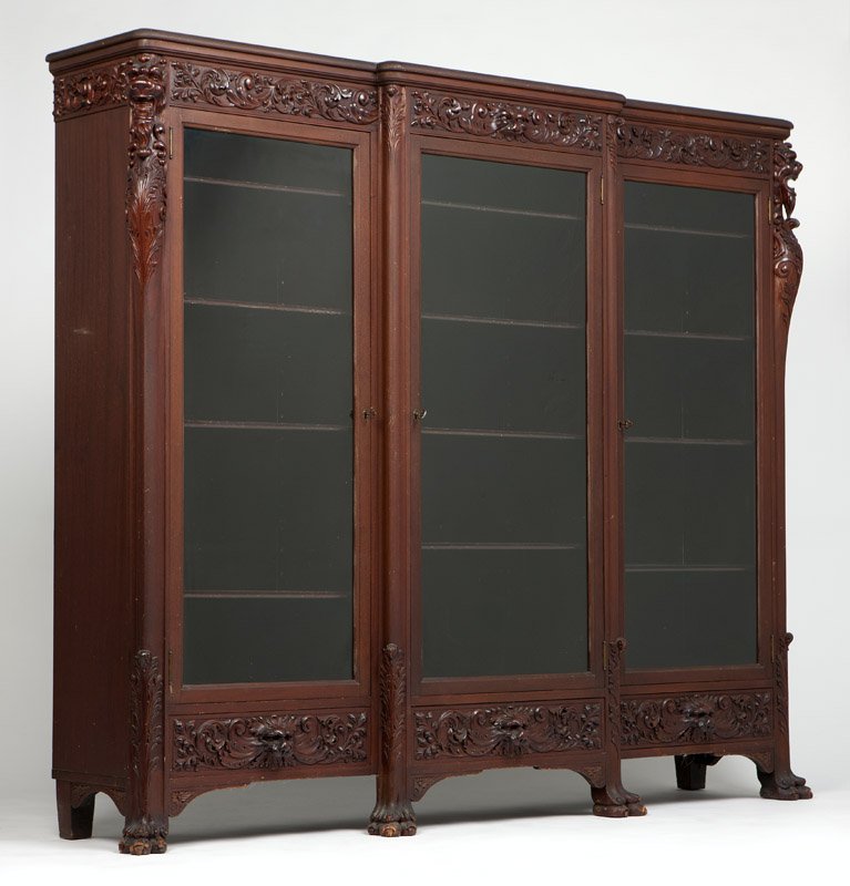 An American carved mahogany breakfront bookcase: Early 20th century, Grand Rapids, MI, with Grand Rapids Furniture Manufacturers Association label, and stamped ''4301'', the molded cornice over a foliate scroll frieze centering a lion's mask, with l