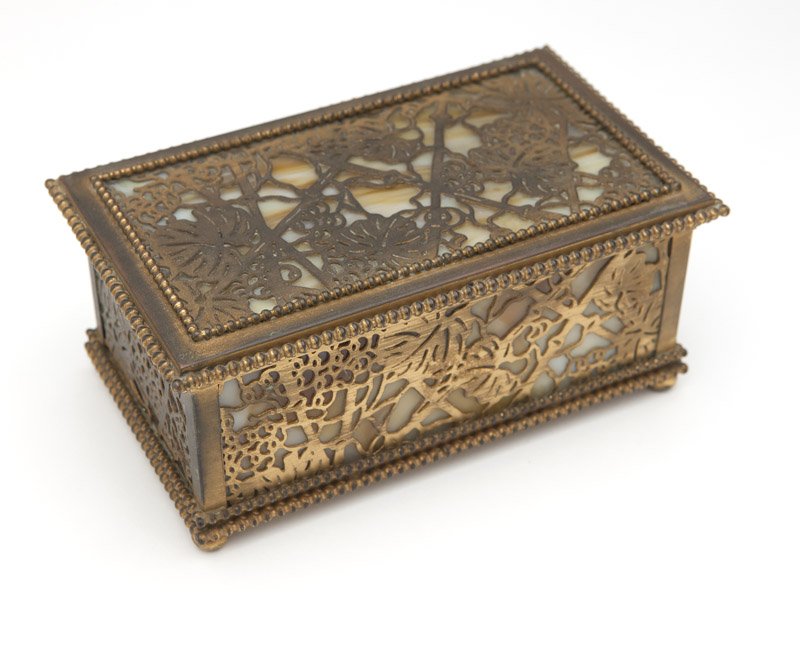 A Tiffany Studios ''Grapevine'' gilt bronze jewelry box: First quarter 20th century, impressed ''Tiffany Studios / New York'' and ''816'', rectangular, the hinged top and sides with pierced panels over caramel-colored slag glass enclosed in beaded borders, 