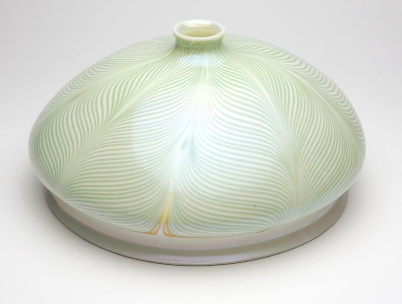 A large Quezal iridescent glass shade: First quarter 20th century, etched signature to fitter rim ''Quezal'', of domed circular form with pulled feather design in green and white with touches of yellow, made for a ceiling fixture, 8.25'' H