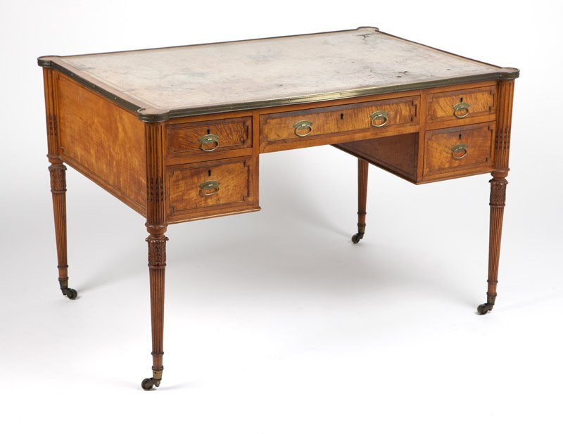 A Sheraton style line-inlaid satinwood writing desk: Late 19th / early 20th century, the eared rectangular top edged with brass molding and inset with a tooled leather writing surface, over a central drawer flanked on each side by two further drawers, e