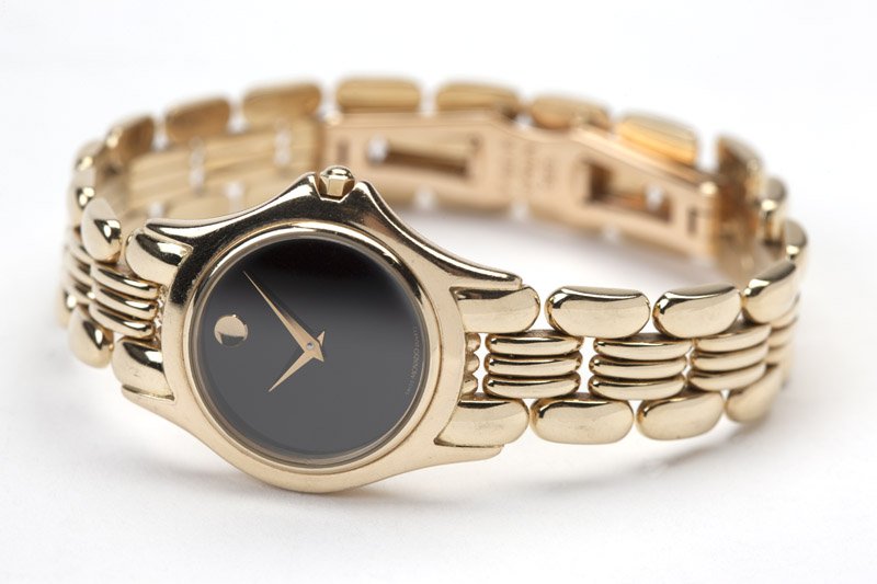 A lady's gold wristwatch, Movado: Circular black dial, gold tone dauphine hands, attached to a quartz movement, within a 14K yellow gold case, Movado, ref: 74-25-840/812300, attached to an integrated gold link bracelet and deployant c