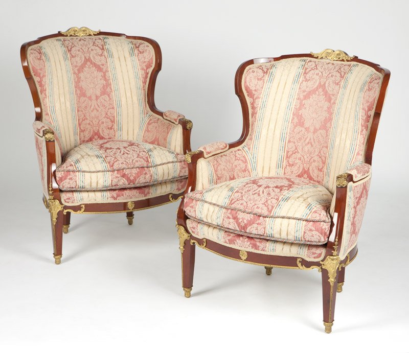 A pair of French gilt bronze-mounted bergeres: First quarter 20th century, each with an arched-back gilt bronze-mounted frame, upholstered with later floral on striped-ground damask fabric, raised on four square tapered legs with columnar sabots, 