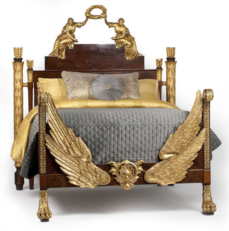 An Empire style gilt and flame mahogany bed: First quarter 19th century and newer, the headboard in two parts, surmounted by opposing carved gilt wood female figures supporting a wreath between them with outstretched arms, the laurel-wrapped pos