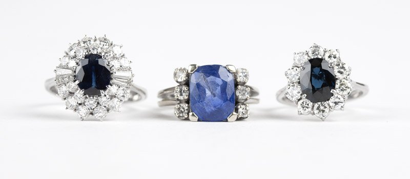 A group of three sapphire and diamond rings: Two 18K white gold and one 14K white gold rings, centering three oval and cushion shaped sapphires totaling approximately 7.75 cts, with a baguette and full-cut diamond surround totaling approximately