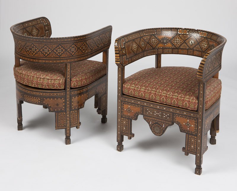 A pair of Syrian parquetry barrel chairs: Second half 19th century, each all-over inlaid with mother-of-pearl, bone, and various fruitwoods, with a rounded back enclosing a conforming seat with upholstered drop-in cushion, the slender squared