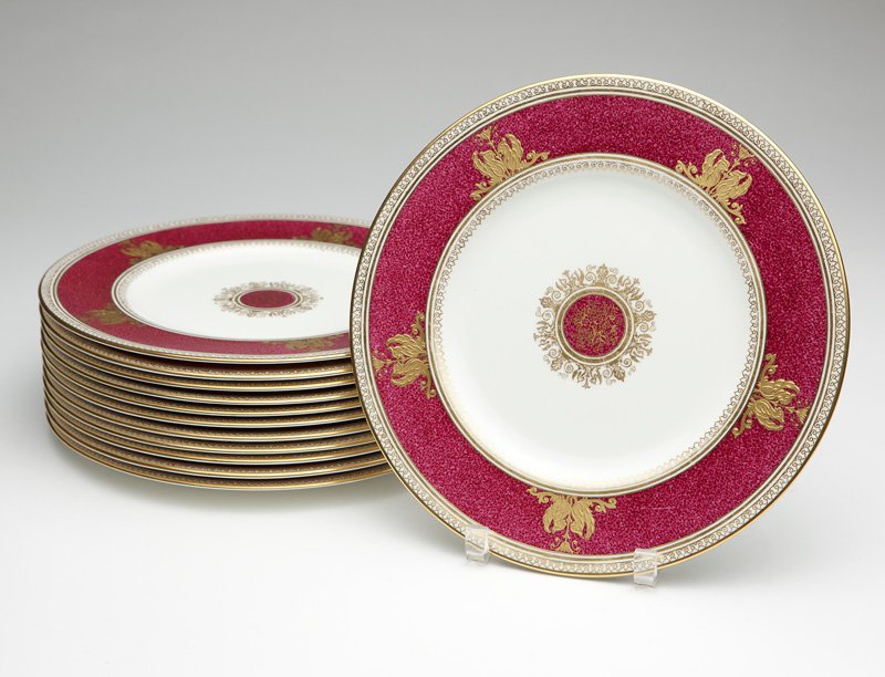 12 Wedgwood china ''Columbia'' dinner plates: 1950-1962, each with maker's mark ''Wedgwood / Bone China / Made in England'', each circular white ground plate with a ruby red rim gilt-painted with facing pairs of dragons, centering a ruby red meda
