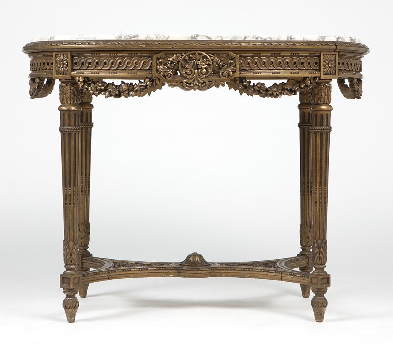 A Louis XVI-style carved and giltwood table: Late 19th/early 20th century, with an inset oval white marble top over a pierced guilloche frieze centering a pierced foliate reserve suspending garland pendants, raised on acanthus-wrapped tapering f