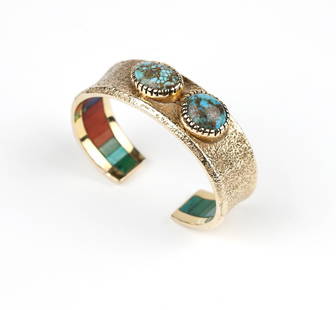 A Hopi gold cuff bracelet, Charles Loloma: Signed for Charles Loloma, a 14K gold tufa-cast cuff bangle with two off-center bezel set turquoise cabochons, interior inlaid with channel-set turquoise, coral and lapis lazuli, opening: 7/8'', overa