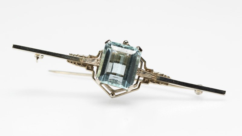 An aquamarine and white gold bar pin: A 14K white gold bar brooch centering a rectangular aquamarine measuring 13.7 x 12.1 x 6.9 mm, weighing approximately 8.15 cts., length 2 3/4'', est: $400/600