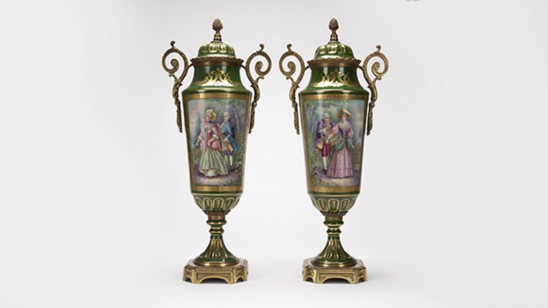 A pair of French Sevres-style lidded urns: Early 20th century, each with gilt intertwined ''L''s enclosing ''S'' over ''France / Hand Painted'' to underside and signed to one reserve ''Guy'', each with a pinecone-form finial over a dual-handle