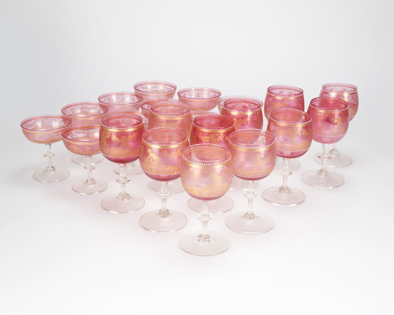 A set of Venetian glass wine and champagne stems: Early 20th century, each pink glass bowl with applied white ''jewels'' and gilt decorated with continuous scenes of Bacchic putti, atop a knopped clear glass stem raised on a spreading circular foot, 