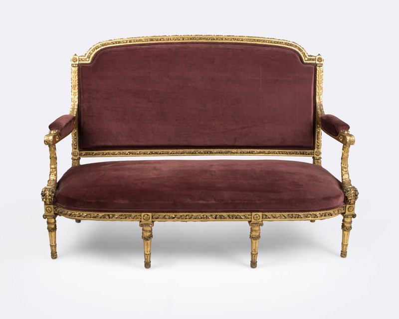 A Louis XVI-style carved giltwood settee: Second half 19th century, the curved back elaborately carved with rope molding and twisted floral and ribbon garlands, issuing acanthus-carved arms raised on cornucopia supports flanking an outcurved 