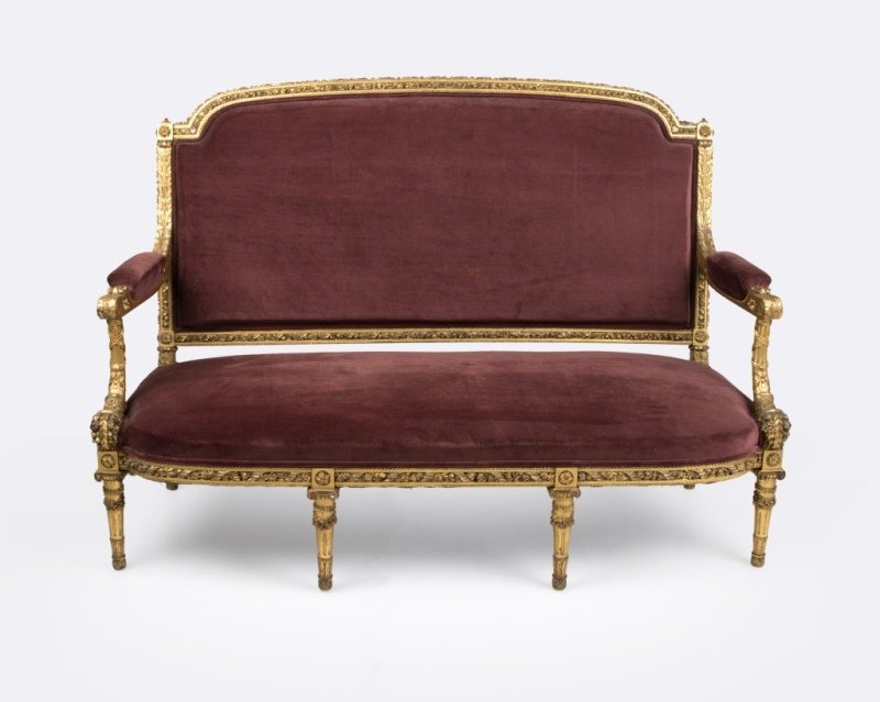A Louis XVI-style carved giltwood settee: Second half 19th century, the curved back elaborately carved with rope molding and twisted floral and ribbon garlands, issuing acanthus-carved arms raised on cornucopia supports flanking an out-curved