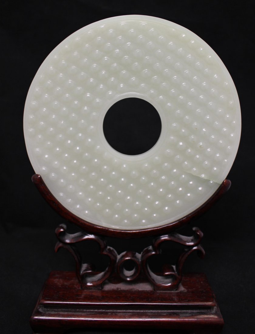 A Chinese large and extremely rare white jade Bi disc: A Chinese large and extremely rare white jade Bi (璧) disc with grain patterns on a wooden stand, 19th century. Diameter :15.8cm(6in) 清 白玉壁