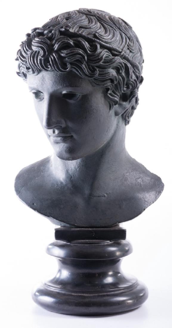 Alva Studios 1955 Bust of Apollo: Cast iron bust depicting Apollo, the Greek god of music and the sun, painted to resemble oxidized bronze and on a sculpted black base. Marked “Alva Studios 1955” to the back of the bust. Bust meas