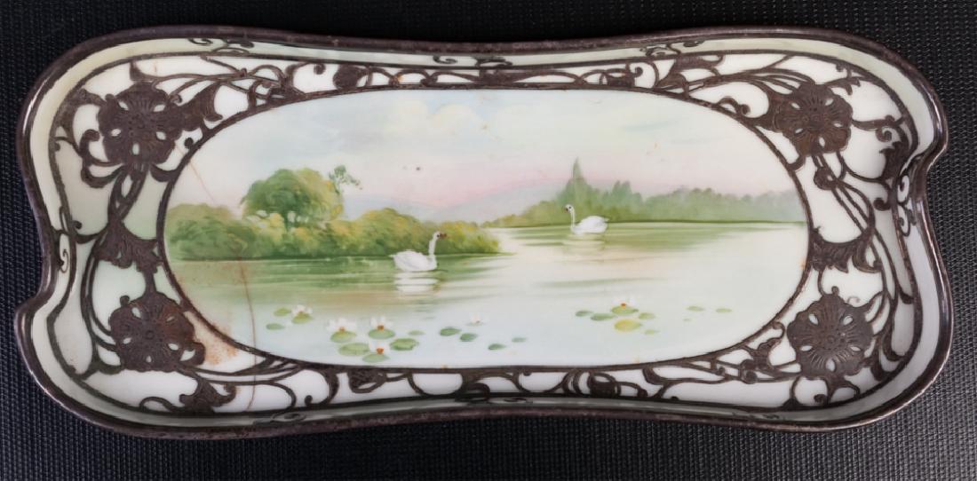 Noritake Nippon Tray w/ Silver Overlay: Noritake Nippon small tray or under plate with a hand painted scene of swans on a lake with silver overlay; measures approximately 5/8” high, 8-3/4” wide and 3-1/2” in depth. Marked to bottom. W