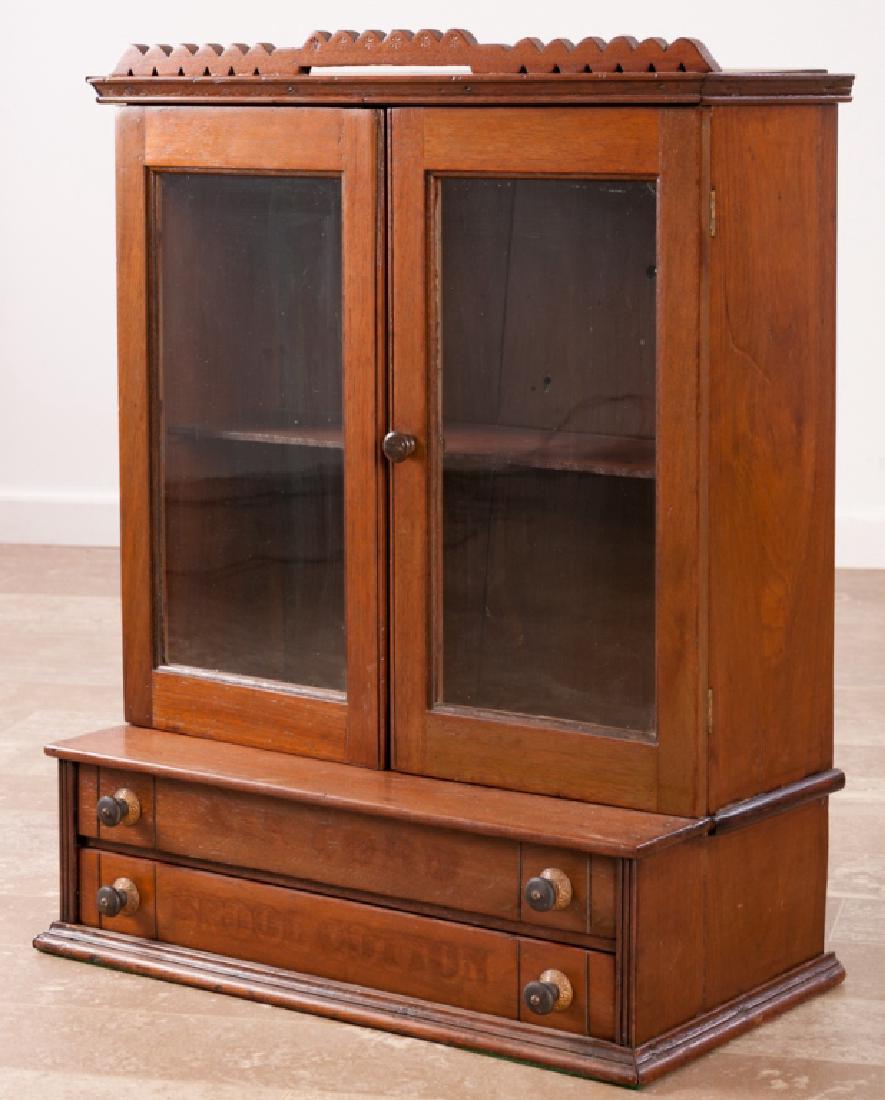 Walnut Cotton Spool Display Cabinet: Early 20th Century walnut store display and spool cabinet having two glass front doors opening to two shelves, original hardware, and faint remnant of “Six Cord Spool Cotton” to the lower drawers;