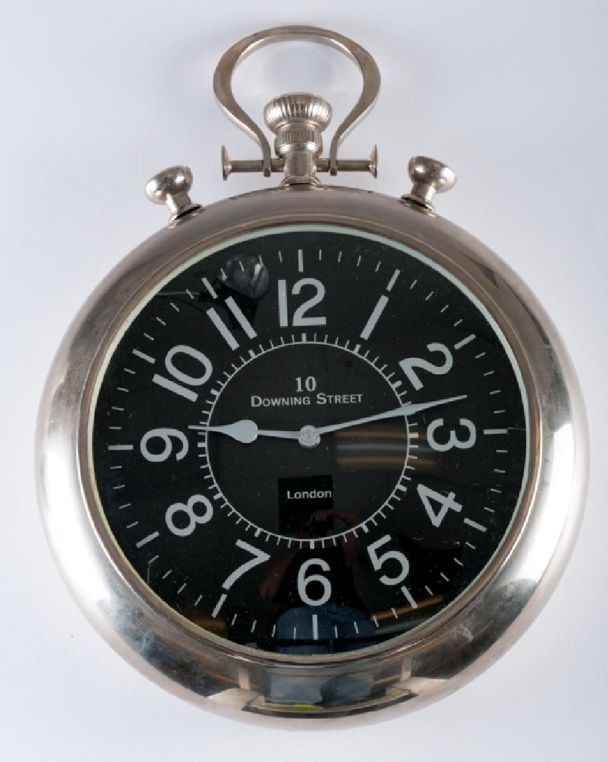 "10 Downing Street, London" Wall Clock: Unpainted metal wall clock in the shape of an analog stopwatch with silver colored hands and numbers on a black dial with “10 Downing Street London” to the center; measures approximately 20” hig