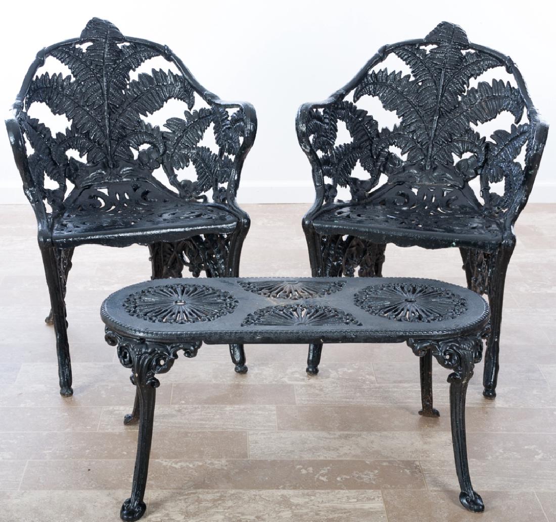 Vintage Cast Iron Patio Set: Three-piece black painted cast iron patio set to include: two (2) chairs with fern leaf pattern backs and open fretwork seats, together with bench / table having open fretwork to the top. Chairs measu