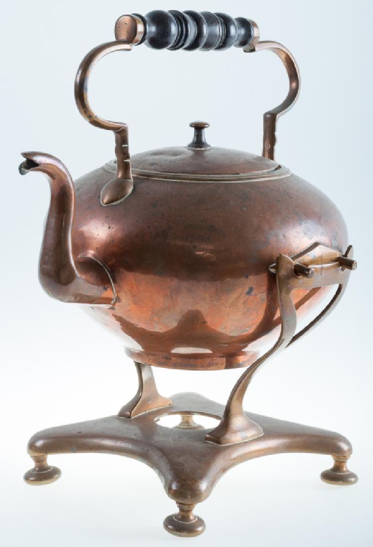 Copper Tea Kettle on Stand: Tilting copper tea kettle with wooden handle, together with warming stand, patinated; measures approximately 13" high, 10-1/2" wide, and 7" in depth. Burner not included.