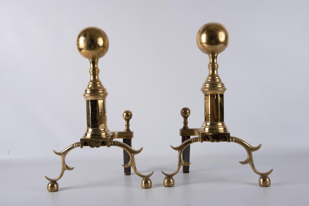Virginia Metalcrafters Cannonball Top Andirons: Pair of Virginia Metalcrafters brass andirons, each having a cannonball top on an octagonal plinth, and spurred legs. Stamped VM for Virginia Metalcrafters. Measure approximately 18-3/8" high, 12-3/8"