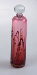 1986 John Abbott Studio Glass Perfume Bottle: Auckland, New Zealand. Cylindrical bottle of cranberry with dark maroon trailing and a clear glass stopper. Chip to rim, signed to base. Measures 6-1/4" high. All measurements are approximate. From th