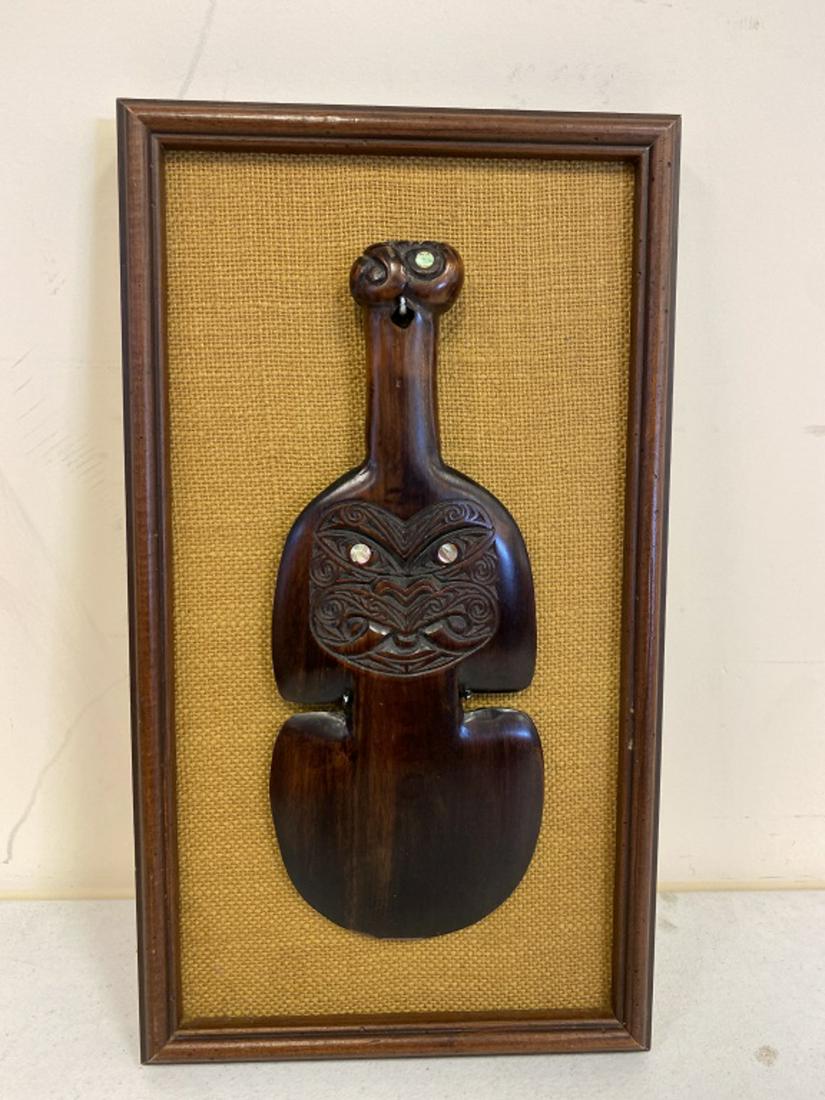 Maori Carved Hand Club: Also called Kotiate paraoa, has paua shell eyes to the face and pommel. Of exotic hardwood. Club measures 13-1/2" long, 5-1/4" wide. Frame measures 18-1/4" high, 10-1/4" wide.. All sales are subject t