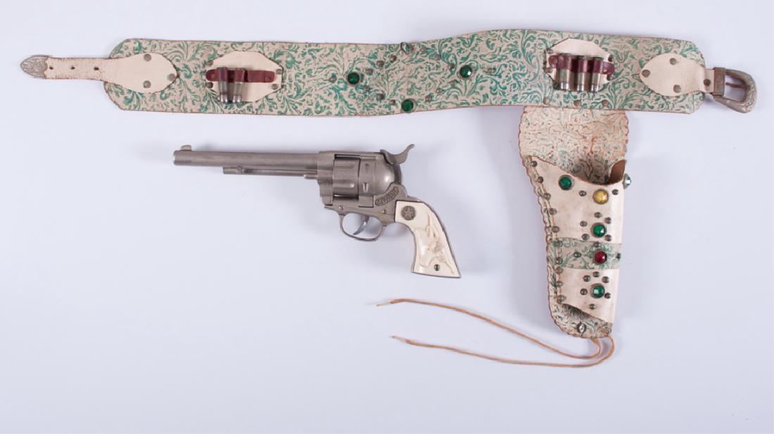 Hubley Cowboy Cap Gun with Holster: Hubley diecast "Cowboy" cap gun with Texas Longhorn and star grips, together with a decorated belt and holster. Toy gun measures 11-3/4" long; belt and holster measures 31" long. Gun marked Hubley to