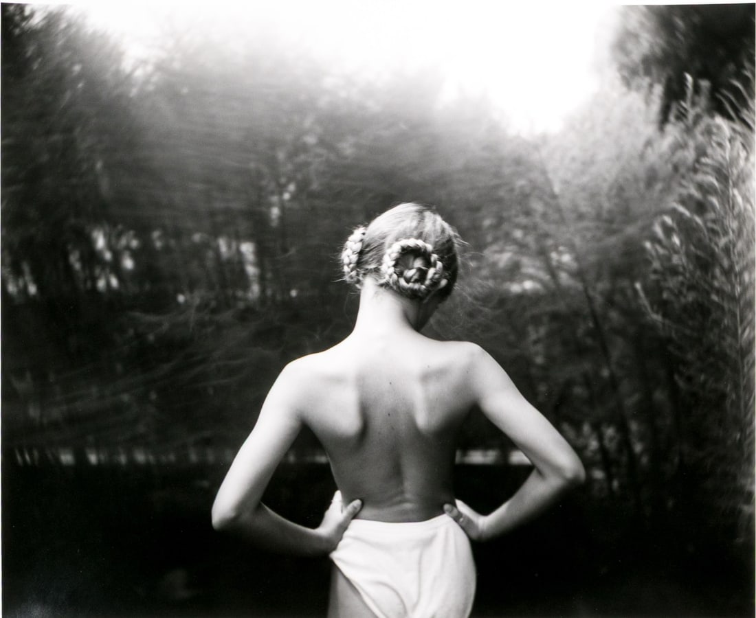 Sally Mann (American, B. 1951) "Vinland, 1992" Signed Gelatin Silver Print: Sally Mann (American, b. 1951) "Vinland, 1992" gelatin silver print depicting a girl with blonde braided hair pinned in loops, posed standing facing away from the viewer with hands resting on her hips