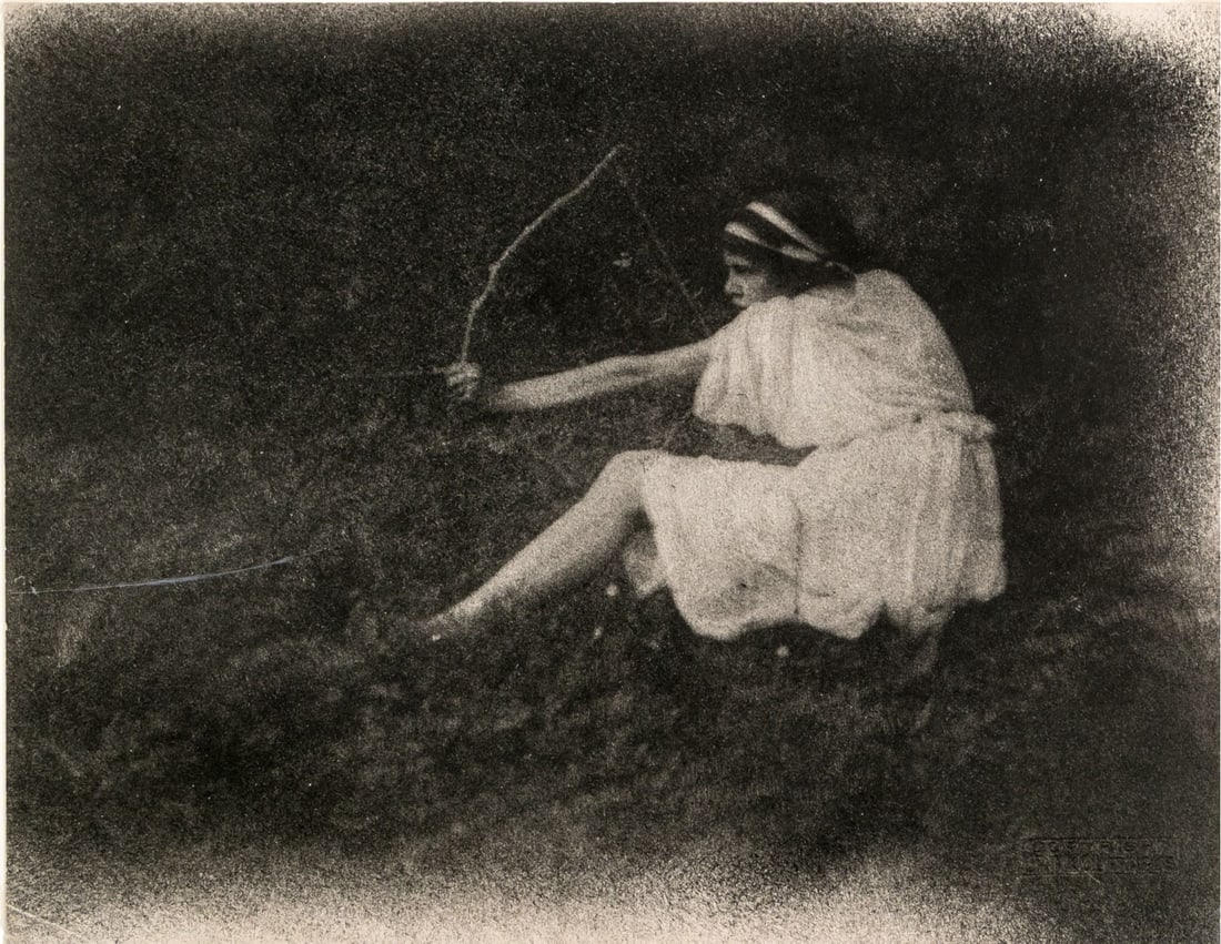 Frantisek Drtikol (Czech, 1883-1961) "The Archer" Ca. 1919, Bromoil Print: Frantisek Drtikol (Czech, 1883-1961) "The Archer (1919)" bromoil print depicting a woman with dark hair wearing a headband and white dress seated in a grassy field in profile, pulling a bow and arrow