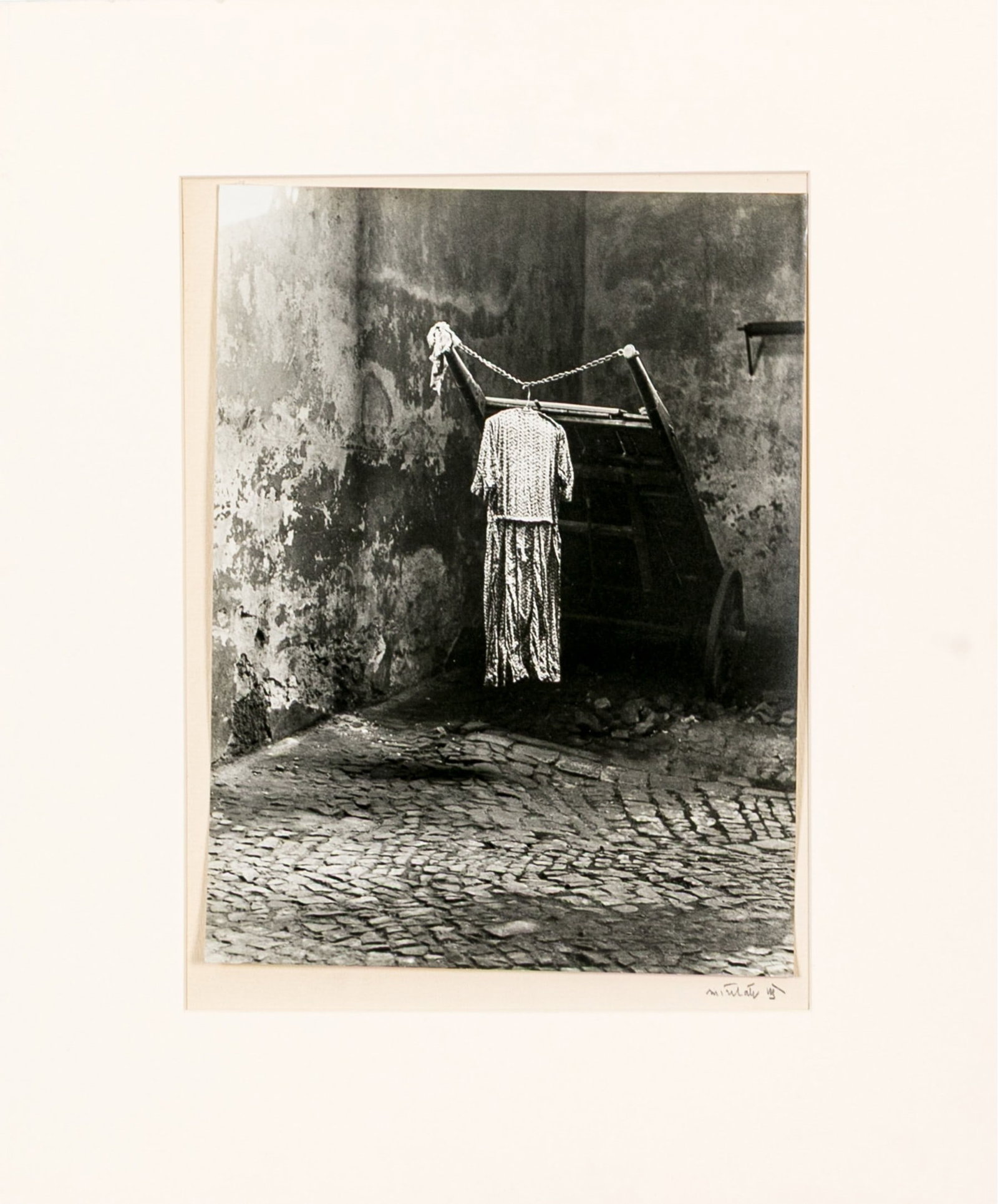 Miroslav Hák (Czechoslovakian, 1911-1978) "Town Corner" (1942) Signed Gelatin Silver Print: Miroslav Hák (Czechoslovakian, 1911-1978) "Town Corner" gelatin silver print depicting a dress on a hanger hanging from a rope tied to a wooden handcart at the corner of a stone paved street. Pencil 