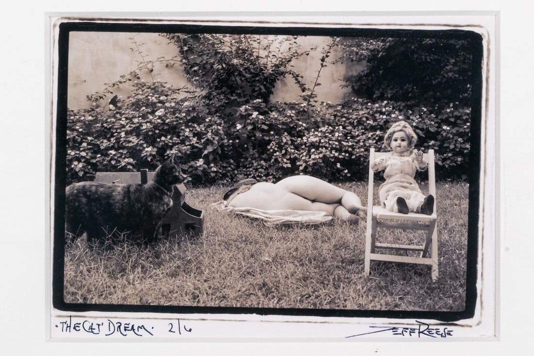 Jeff Reese (American, D. 2008) "The Cat Dream" Signed Gelatin Silver Print: Jeff Reese (American, D. 2008) "The Cat Dream" Signed gelatin silver print depicting a female nude napping in a garden along a hedge of flowering bushes while a cat in profile looks towards a doll sea