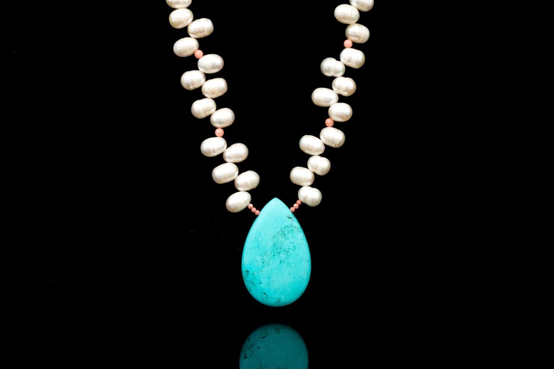 DECORATIVE CULTURED FRESHWATER PEARL, CORAL AND HOWLITE NECKLACE WITH STERLING CLASP: This decorative cultured freshwater pearl necklace has a fringed effect and is decorated with small coral beads and adorned with a chunky pear shaped howlite center. The necklace is finished with ster
