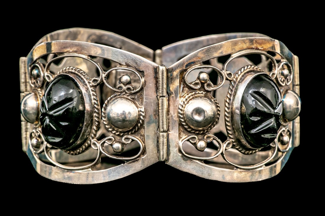MEXICO STERLING SILVER INTENSE BLACK OBSIDIAN WARRIOR MASK PANEL BRACELET: This intense sterling silver bracelet, made in Mexico, features four curved and hinged panels, decorated with a carved black obsidian warrior mask (which represents protection, and the heart of the