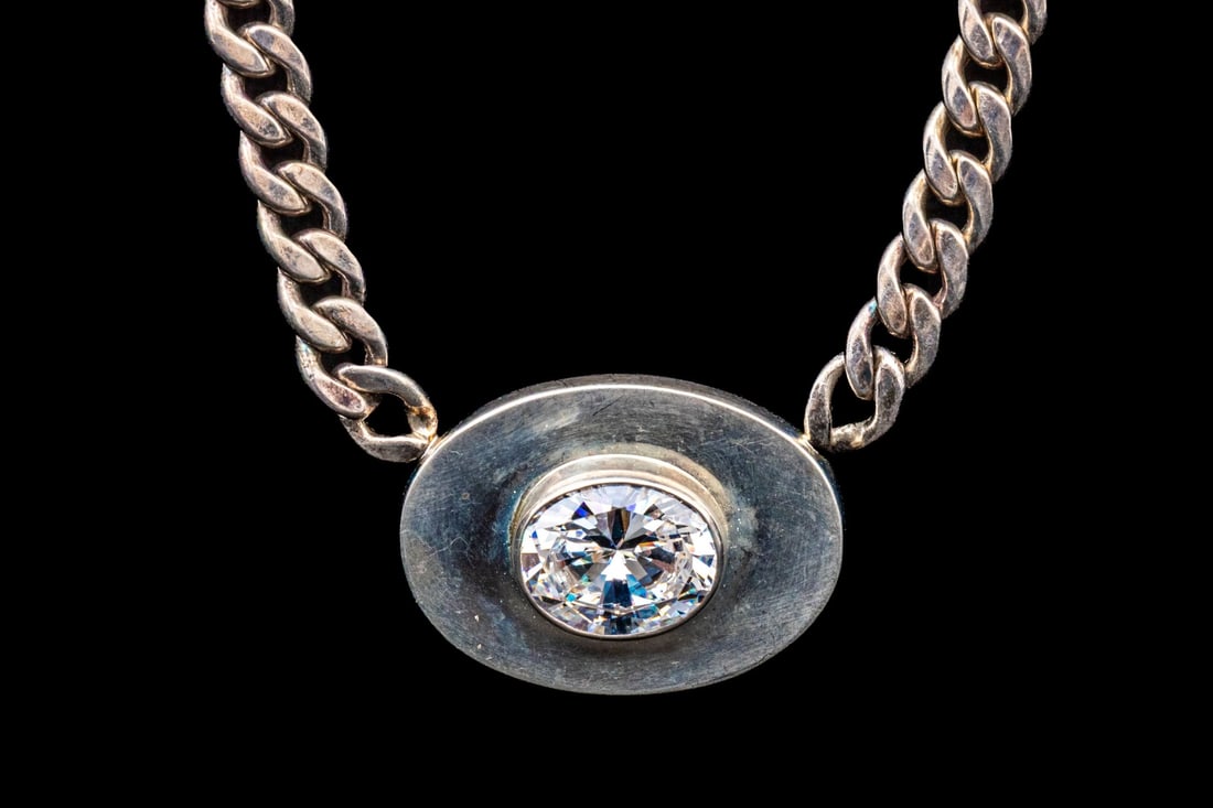 STERLING SILVER BEDAZZLED LARGE OVAL BRILLIANT CZ SET NECKLACE: This sterling silver bedazzled large oval brilliant CZ set necklace features a bezel set center, atop a step cut plinth, decorated with a high polish. The necklace is displayed on a chunky, curb link 