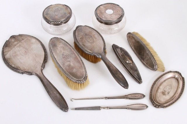 DRESSER SET 10 PEICE STERING SILVER MOUNTED: Comprising of a hand mirror (13" long), powder jar, hair receiver, two brushes, pin tray (5 3/8" long), nail file and buff, three brushed (in fair condition), and a hook. Expected wear, Ca 1920's