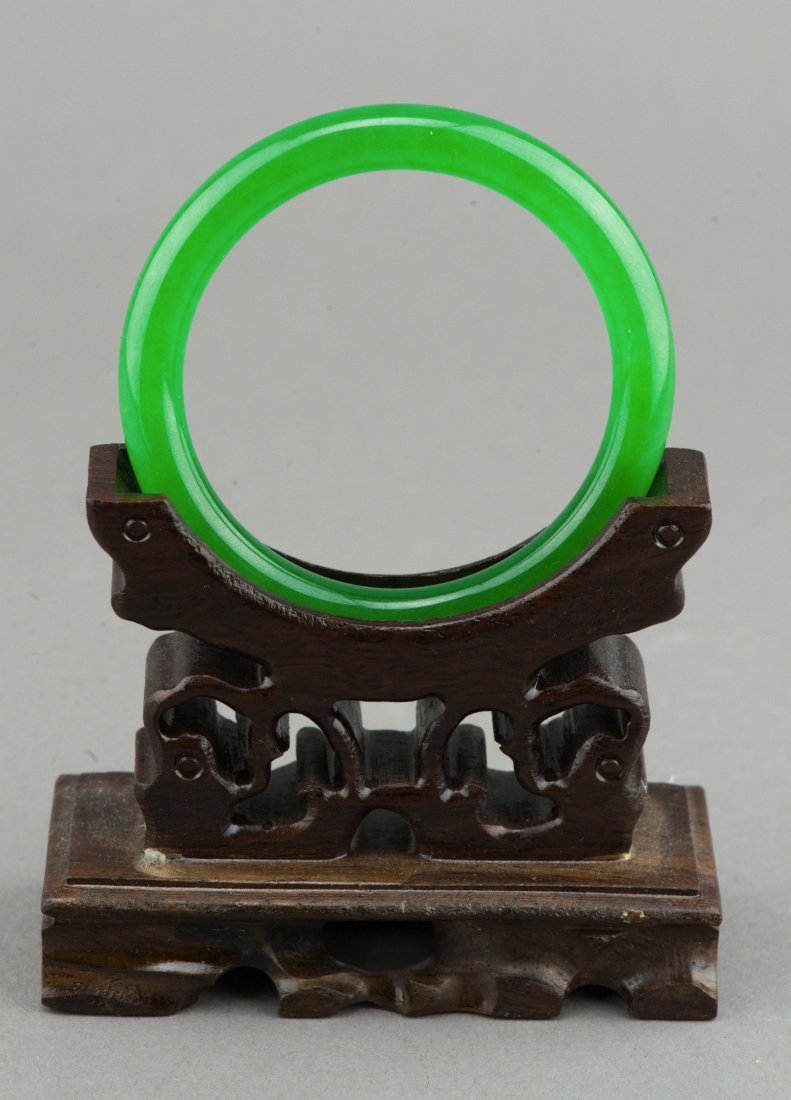 Important Chinese Emerald Green Jadeite Bangle: Chinese jadeite carved circular bangle, of even emerald green tone, rounded edge with fine polished finish. Wooden stand not included. 2.36" (6.0 cm)