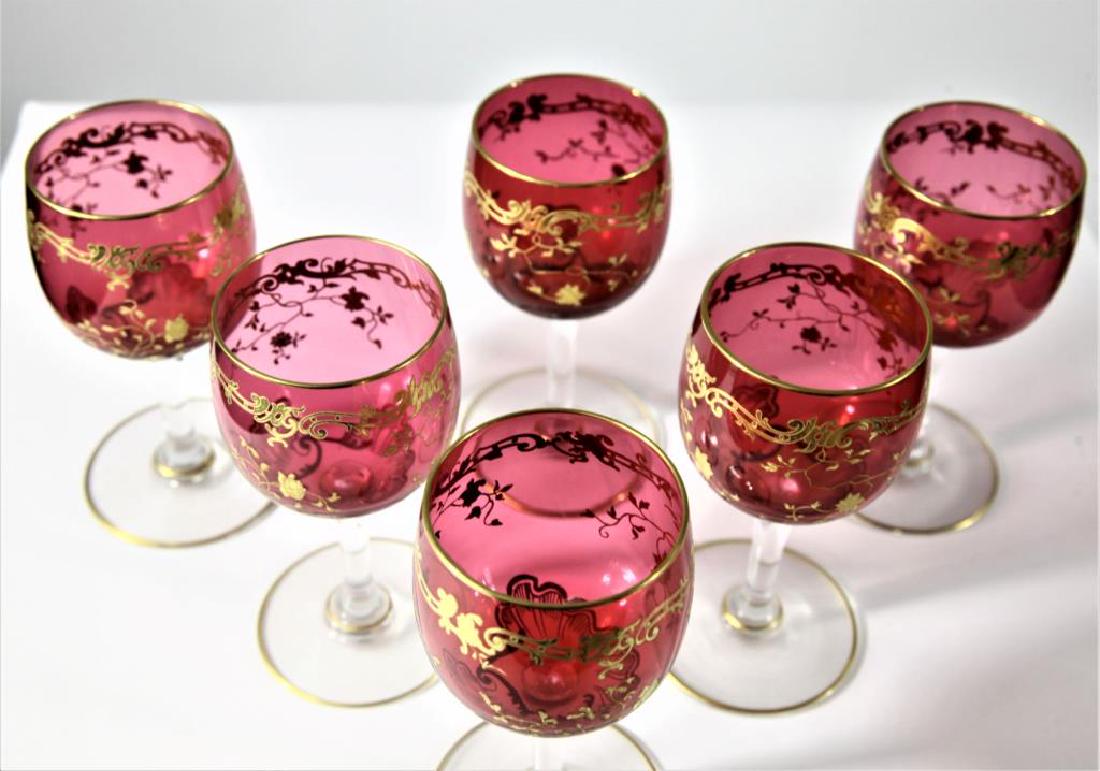 (6) Cranberry wine glasses, Moser-type: Six (6) cranberry wines with clear crystal stems, gold enameling and gold enameled decorations, Moser-type, 4 13/16” h x 2 1/2” base