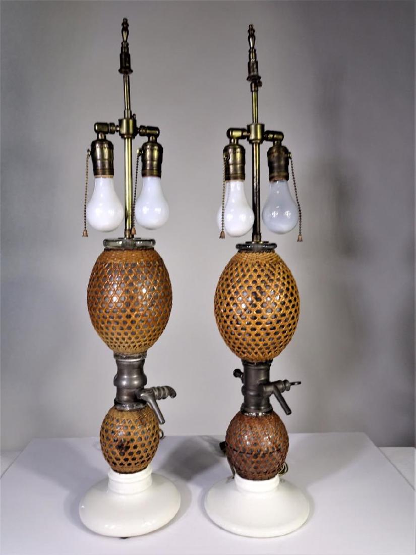 Pair of Antique French Gazogene Briet Table Lamps: Seltzer dispensers, circa 1875-1890, the glass globes covered in cane webbing, the dispenser lever stamped "Gazogene Briet," the collar "2 Boutelles"on white porcelain bases, now mounted as lamps. 20.