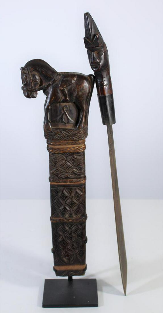Sumba Knife, Indonesia: Knife and scabbard from Sumba, an island in eastern Indonesia. The scabbard is comprised of a carved wood horse at the top of an elaborate geometric carved design, mounted on a steel base. The knife h
