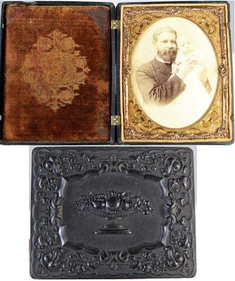 U.S. Union Case, Half-Plate (Krainik 13) 1850's: This is a large thermoplastic union case with an ambrotype of a family scene, probably father and child. The ambrotype is a half plate, and the embossed covers feature a fruit bowl with still-life, a 