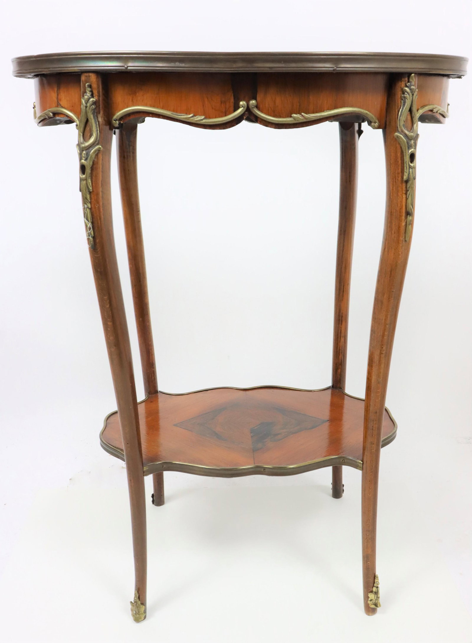 Antique French Table w/ Bronze Mounts: Gilt brass mounted table having an oval top and a low shelf. Inlaid top cabriel legs terminating in a scroll foot. Condition good. Size: 22 x 14 x 29 in. Please note that all sales are final. No refun