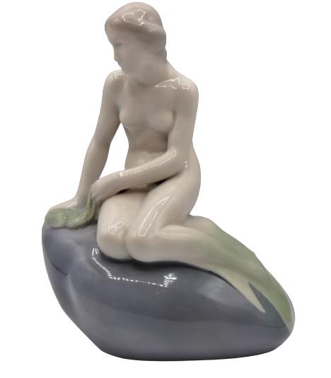 Edvard Eriksen Royal Copenhagen Porcelain Mermaid: This is a Royal Copenhagen porcelain mermaid. On the side is the name Edvard Eriksen, who is the artist that made the original bronze statue of this figure. The original sculpture is bronze and sits o
