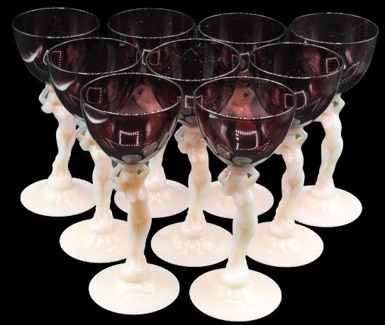(9) Nude Figure Stemmed Cocktail Glasses, c. 1930: Nude Figure Stemmed Wine Glasses, c. 1930. 9 Cambridge Glass Company Cocktail Glasses. The glass is of a red hue and the stems are cream colored. Size: 2 3/4 x 6 3/4 in. #1696