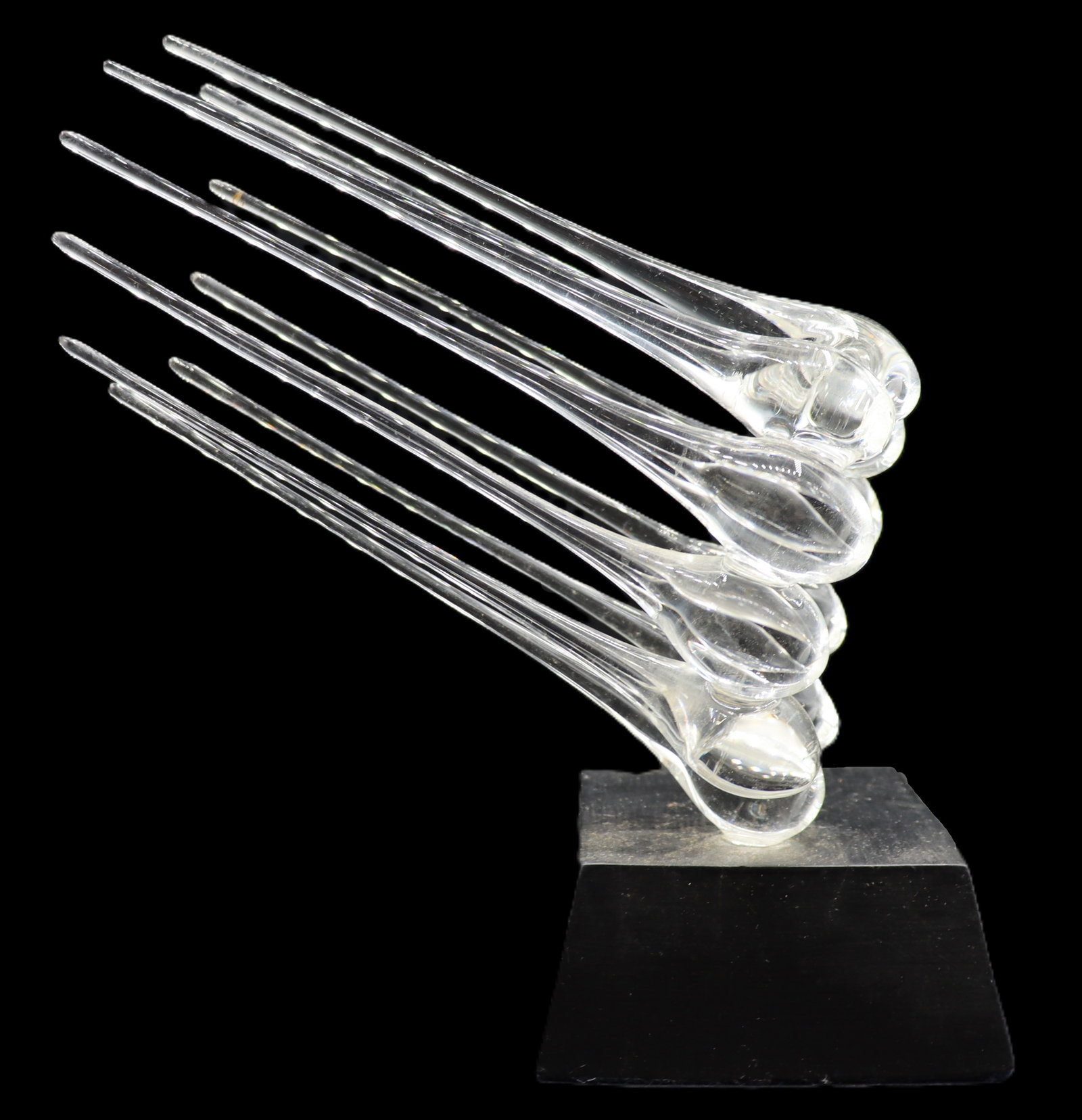Frabel Art Glass Abstract Sculpture on Stand: Frabel Art Glass Abstract Sculpture on Stand. Abstract blown transparent art glass sculpture of a collection of ten elongated droplets arranged in an oval. Balanced on a diagonal angle on a polished b