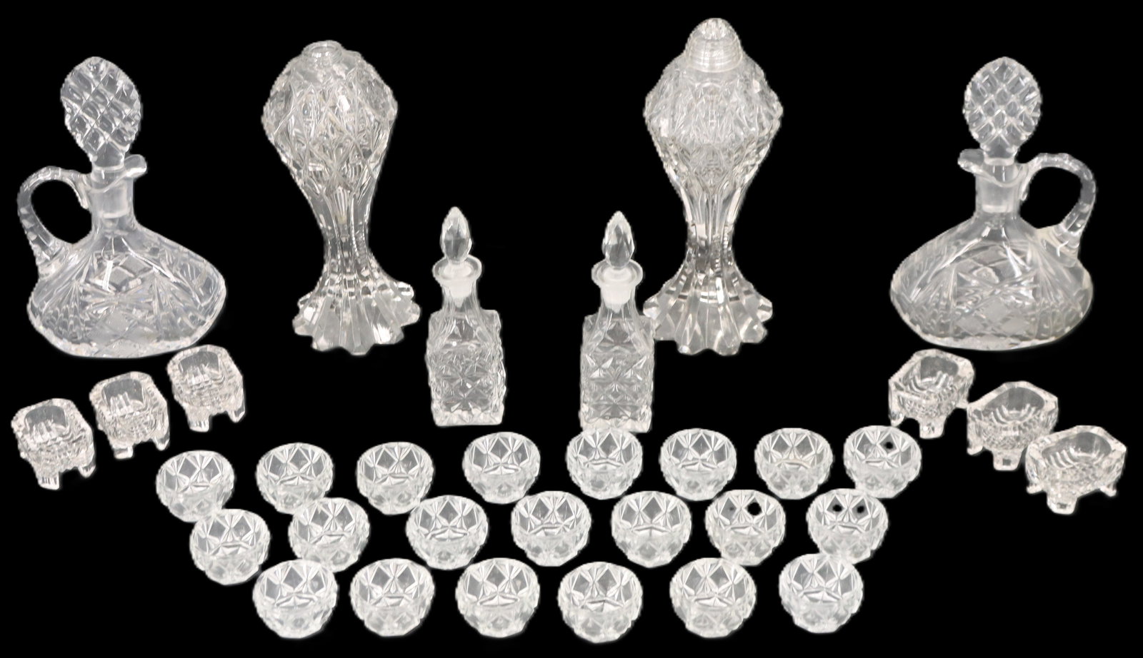 (33) Cut Crystal Serveware Pieces: (33) Cut Crystal Serveware Pieces. Includes 21 small rounded bowls, 6 small footed trays, 2 bottles for oil and vinegar, 2 decanters with large stoppers, and 2 large salt and pepper shakers. Condition