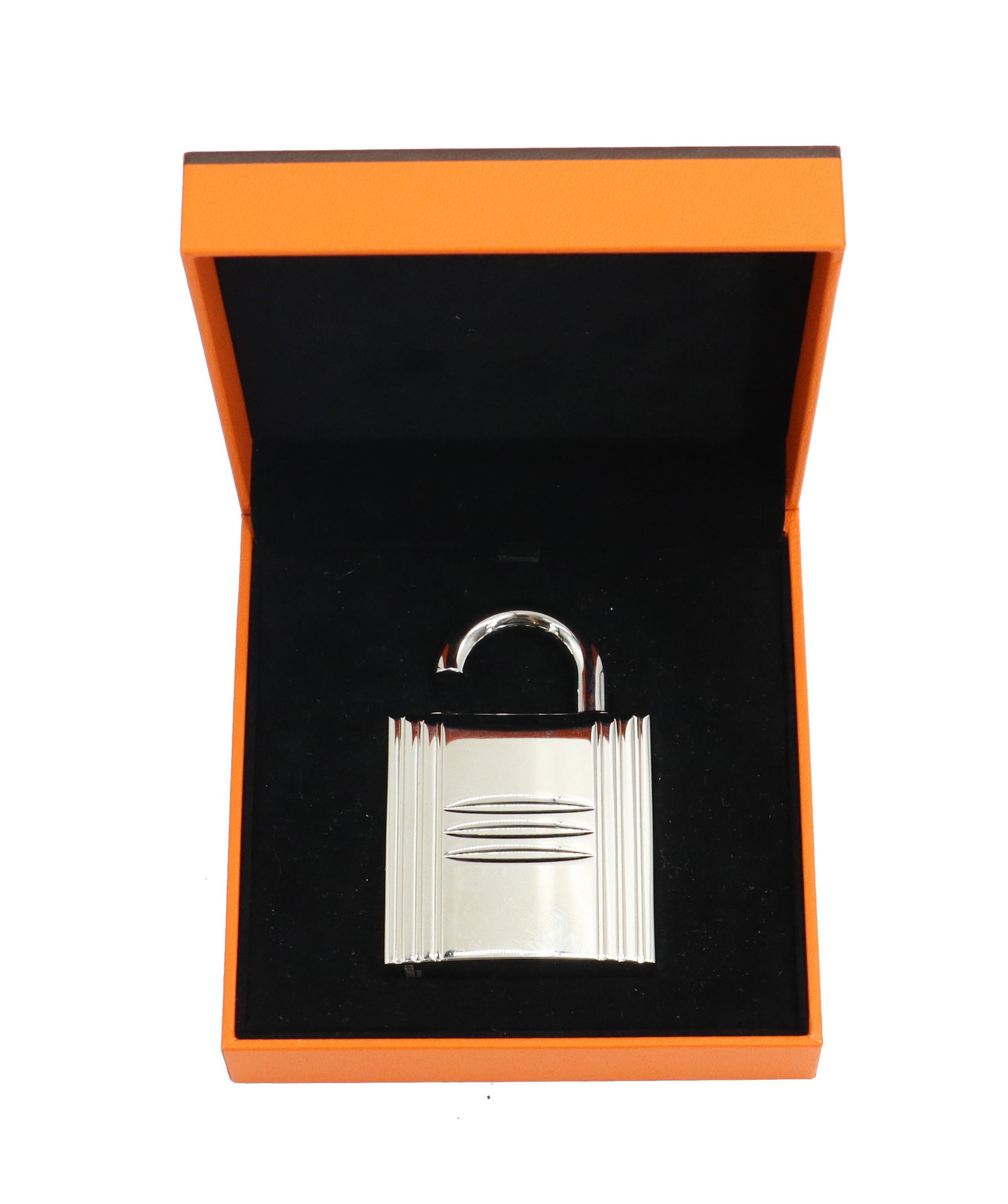 Hermes Cadenas Padlock Perfume Case: Hermes Cadenas Padlock Perfume Case. Silver tone finish. Distinct textured front, characterized by three horizontal grooves and vertical ribbing along the sides. Comes with original box. Size: 4