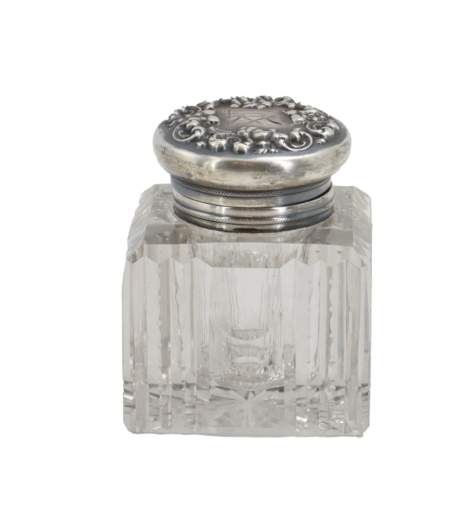Cut Crystal Inkwell with Sterling Top: Cut Crystal Inkwell with Sterling Top. Antique inkwell consists of a heavy, square-cut crystal base paired with an ornate silver-toned lid featuring elaborate floral repoussé work. Size: 4 x 3