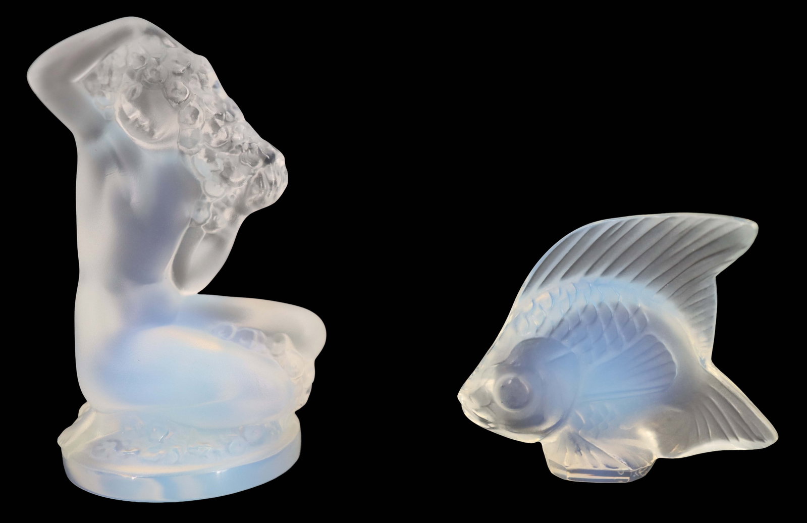 (2) Lalique Frosted Crystal Decorative Figures: (2) Lalique Frosted Crystal Decorative Figures. One is a nude female form kneeling and turned with her hands in her hair, and the other is a small, delicate fish, both with a lightly iridescent sheen.